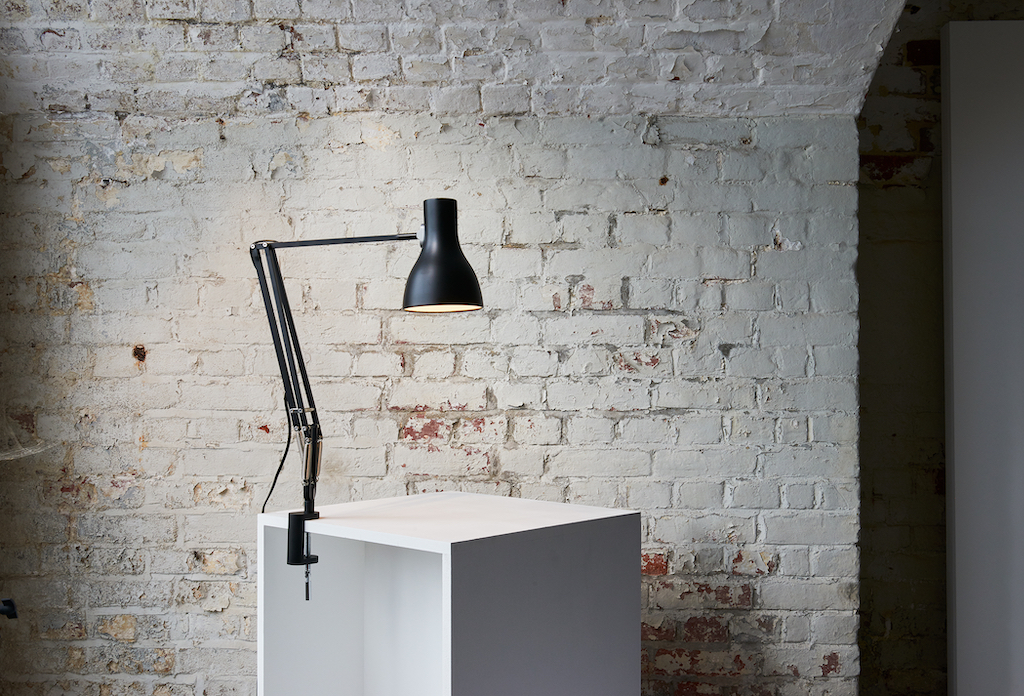 black lamp clamped onto white desk and brick wall in the background